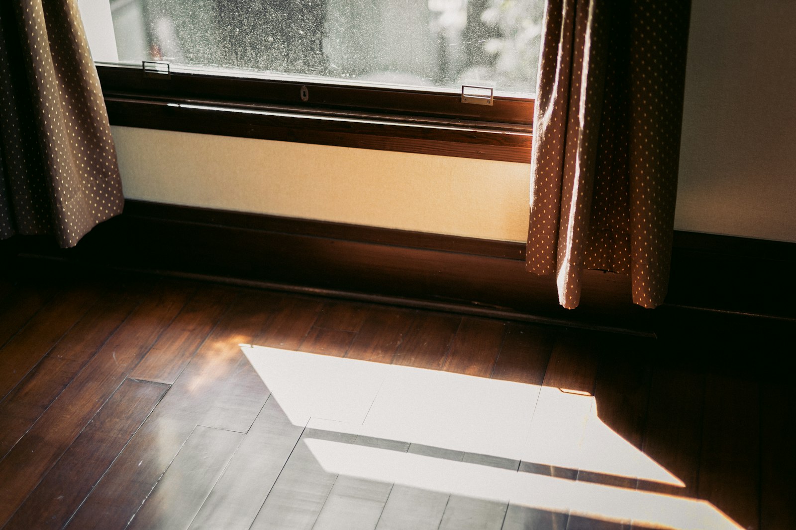 Dark walnut wood floor with a patch of sunlight beside a window