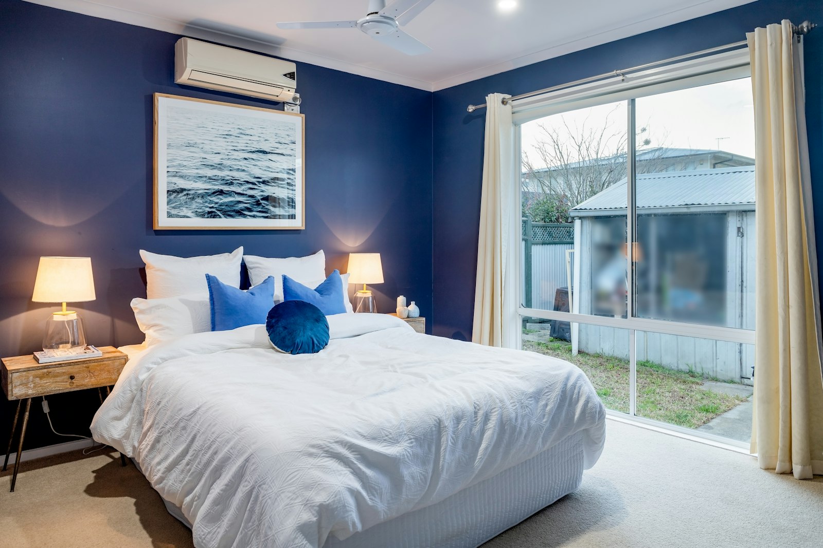 Bedroom with a deep navy blue wall, white bedding and a framed sea photograph